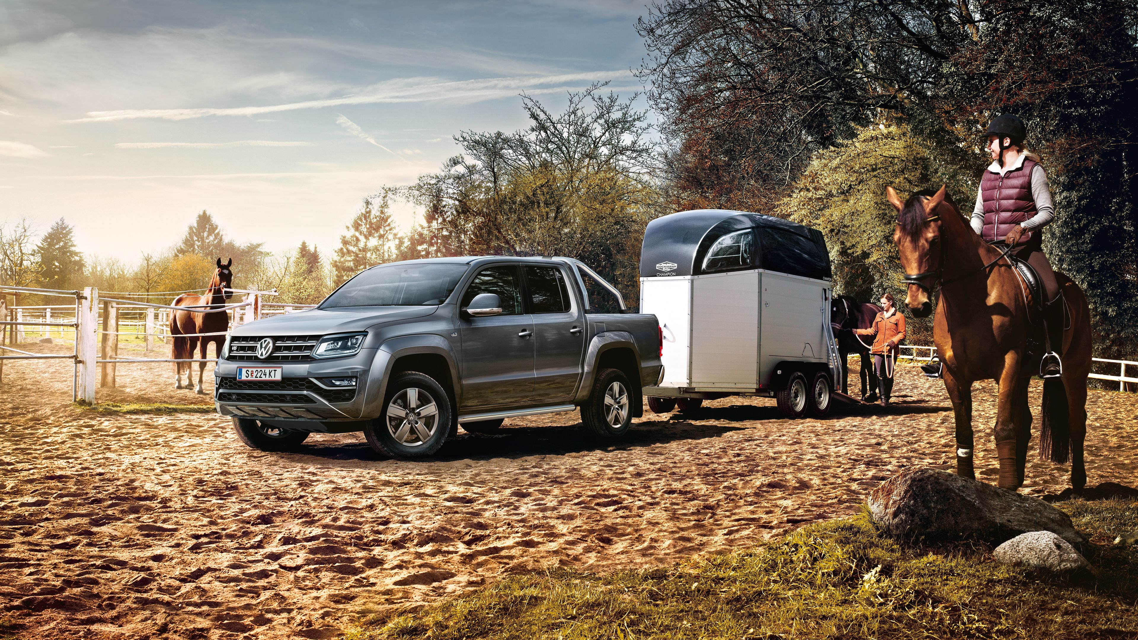 VW Amarok mit Pferdeanhänger und Frau sitzt daneben auf Pferd.