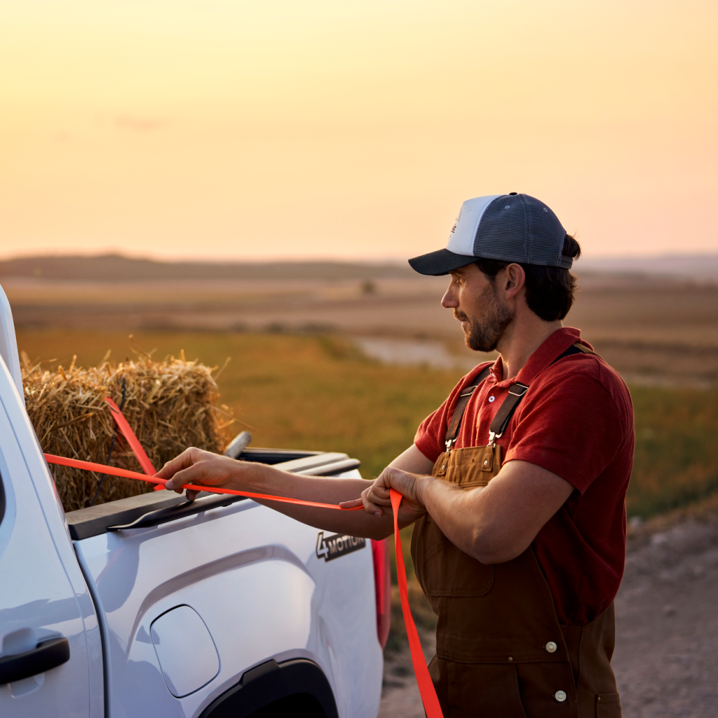 Ein Mann zurrt einen Strohballen an der Ladefläche eines Volkswagen Amarok fest.