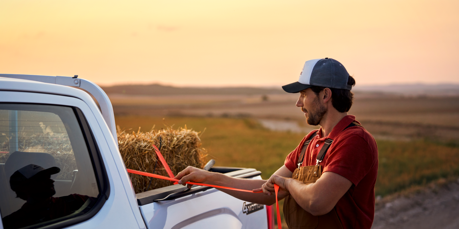 Ein Mann zurrt einen Strohballen an der Ladefläche eines Volkswagen Amarok fest.