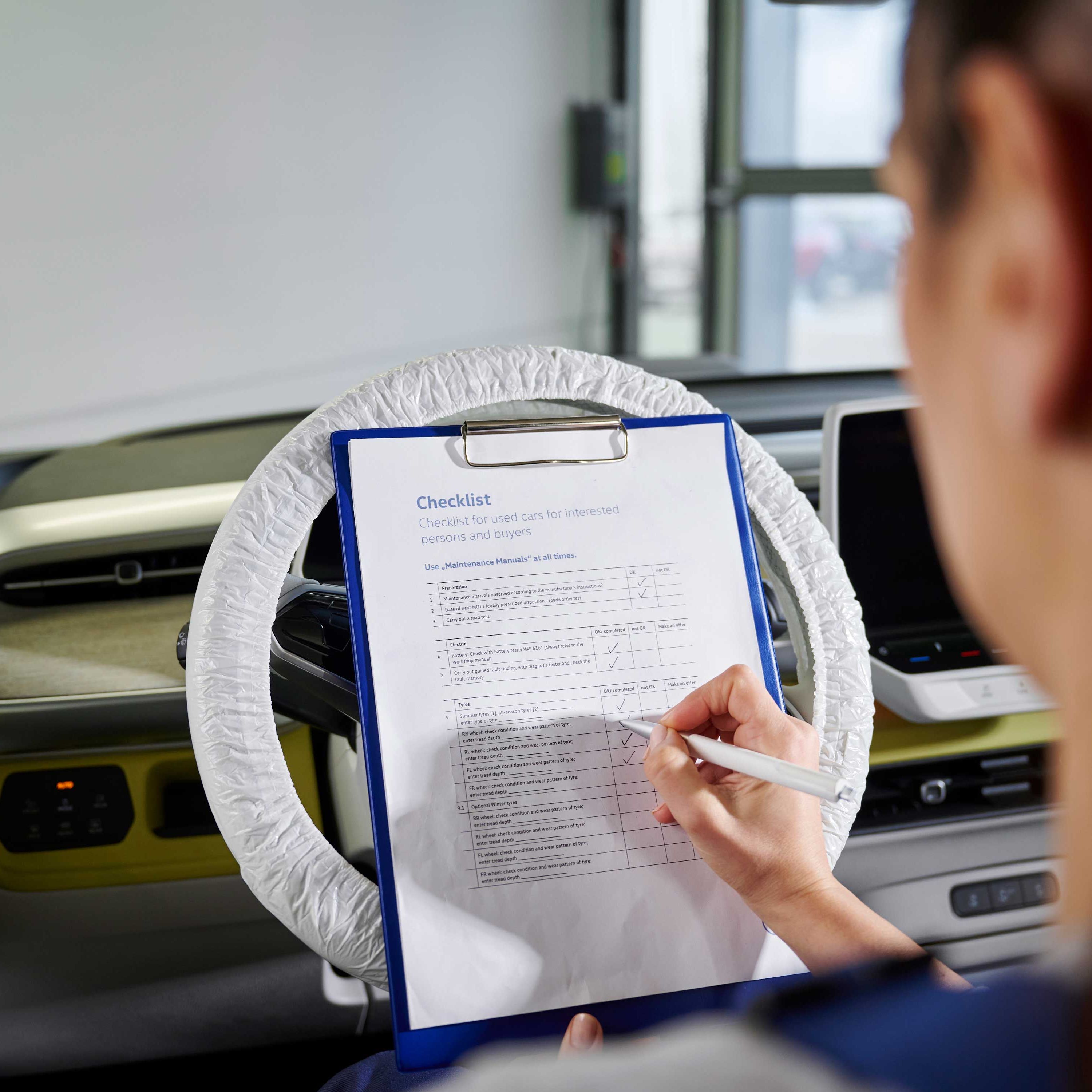 Eine Volkswagen Service Technikerin hakt die Checkpunkte auf einer Liste ab